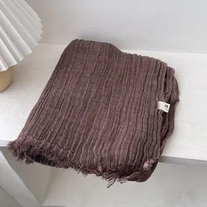 Close-up of deep brown pleated cotton scarf with natural fringe edges and texture