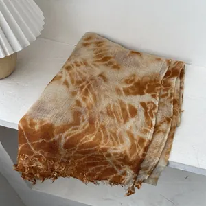 Detail of gradient tie-dye wool shawl with artisan frayed edges on a wooden surface