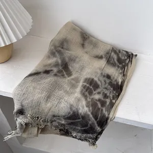 Macro detail of tie-dye wool scarf with artisanal fringe edges on a white wood surface