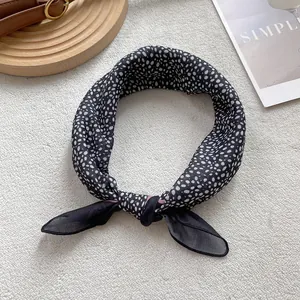Detailed view of black and white polka dot silk scarf tied in a knot on textured base
