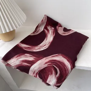 Detail of burgundy scarf with abstract pink swirl pattern and delicate fringe edges