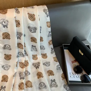 Close-up of cotton linen scarf with cartoon teddy bear patterns on a textured sofa