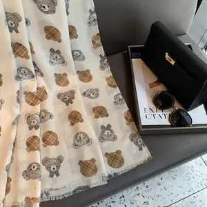 Detail of soft cream-colored scarf with cartoon teddy bear patterns and subtle fringe edge