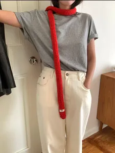 Detail of red thin knit scarf with egg. brand label shown on a casual grey t-shirt outfit