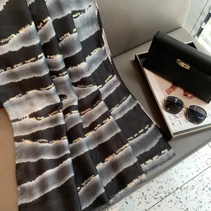 Gros plan sur l'écharpe en dégradé noir et gris avec détails en feuille d'or fin