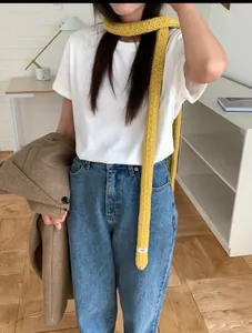 Detail view of ginger yellow skinny knit scarf styled with white tee and denim jeans