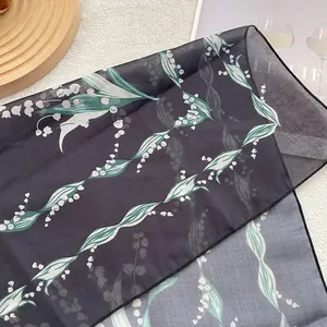 Detail of dark grey scarf with green leaves and white lily of the valley floral pattern
