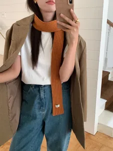 Detail of orange ribbed knit scarf with small white label shown on casual outfit