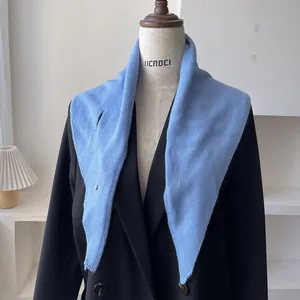 Detalle de bufanda triangular de lana azul claro con hebilla de plata sobre un blazer