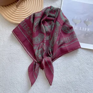 Detail of burgundy square scarf with green paisley patterns and silky fabric texture