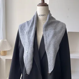 Detalle de bufanda triangular de lana gris que muestra la textura y el pequeño colgante