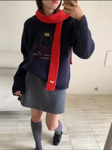 Close-up of red ribbed knit long scarf styled with a navy embroidered academic sweater