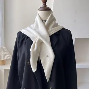 Detalle del pañuelo triangular de punto crema con un elegante botón metálico plateado