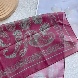 Macro detail of burgundy paisley silk scarf with mint green patterns and stitched edges