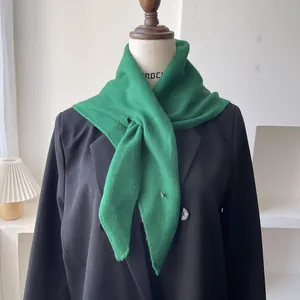 Detalle de bufanda de lana verde con tejido acanalado y pequeño logotipo metálico