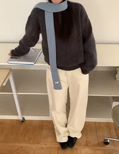 Full body shot of a minimalist skinny knit scarf styled with grey sweater and cream trousers