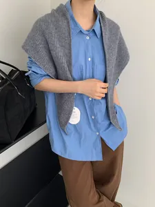 Detail of grey ribbed knit shawl layered over a light blue shirt and brown trousers