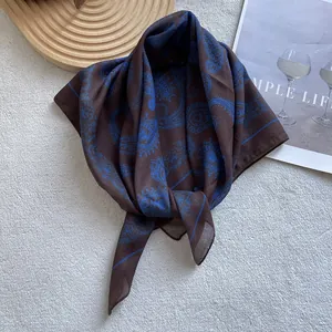 Elegant beige and brown paisley silk square scarf displayed on a soft white texture background