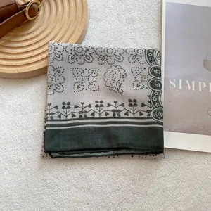 Detailed view of paisley square scarf with fine stitching on a vintage wooden tray
