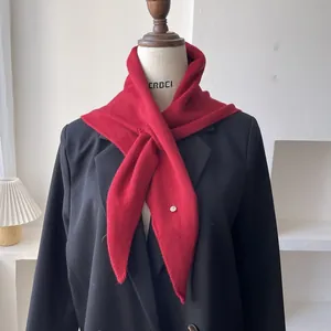 Detalle de bufanda triangular de lana roja con colgante metálico sobre un blazer negro