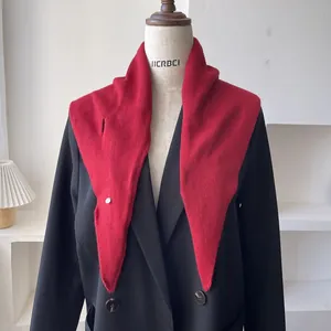 Detalle del chal triangular de punto rojo con botón plateado sobre un blazer negro