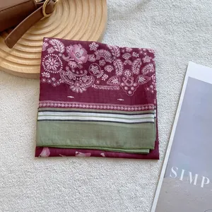 Elegant burgundy paisley floral square silk scarf with striped edge on a wooden tray