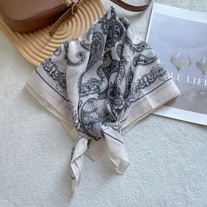 Detail of beige paisley silk square scarf with blue borders on a minimalist display