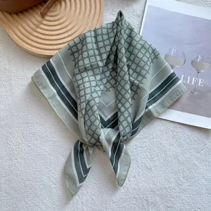 Detail eines eleganten grünen Seidenschals mit geometrischem Muster auf weichem Plüsch