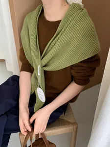 Detail of green ribbed knit shawl with designer tag worn over brown sweater