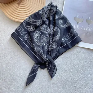 Close-up of black and white paisley silk square scarf on a minimalist lifestyle backdrop