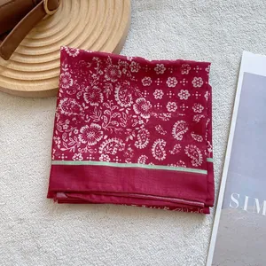 Detail of red paisley silk scarf with green edges folded on a vintage background