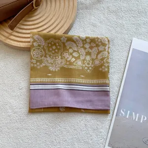 Close-up of paisley floral pattern on ginger yellow silk scarf with purple border details