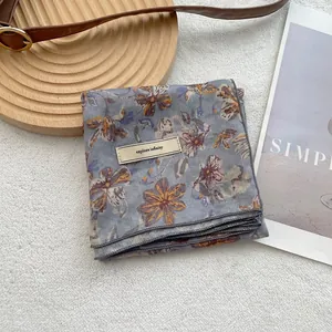 Grey floral silk scarf with yellow and purple flowers on a rustic wooden tray