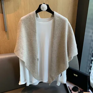 Detail of beige wool knit triangular scarf with mottled texture on a white shirt