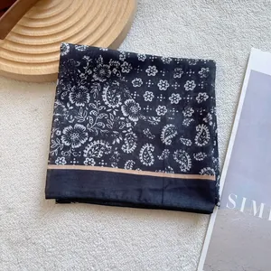 Detail of vintage black and white paisley silk scarf on a soft white plush background