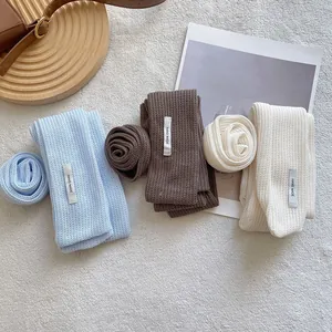 Three knitted flower scarves in blue, brown, and cream with handmade labels on soft fabric