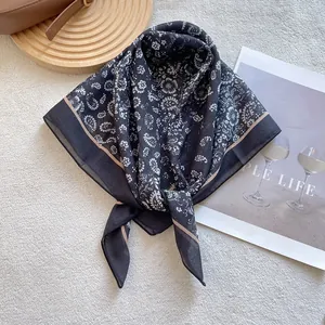 Detail shot of a black paisley square scarf with beige trim on a textured background