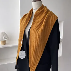 Close-up of ginger yellow ribbed knit shawl featuring a brand tag on a black blazer coat