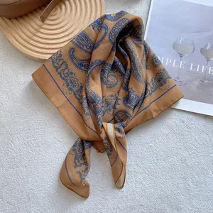 Close-up of beige paisley silk square scarf neatly folded on white textured carpet backdrop
