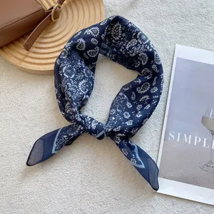 Detail of blue paisley silk scarf tied as a bow on minimalist textured background