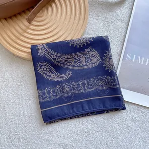 Detail of navy paisley square scarf displayed on white fur with lifestyle props