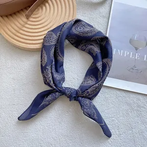 Close-up of a navy silk scarf with beige paisley print on a wooden tray with a magazine