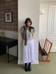 Detail showing grey knit sweater paired with brown scarf and white pleated midi skirt