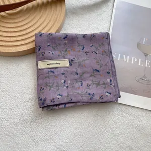Close-up of floral purple silk scarf with explore infinity label on soft white background