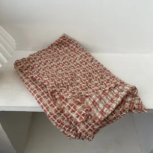 Classic red brown plaid knit scarf with fringed edges on a minimalist white stone surface