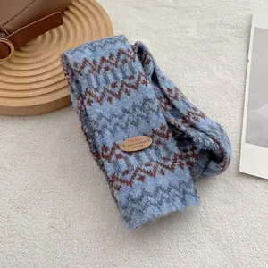 Detail van de Fair Isle gebreide sjaal met blauwe golfpatronen en bruin leren label