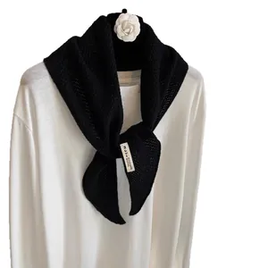 Elegant black knit wool cashmere triangle scarf draped on a white shirt with flower hanger