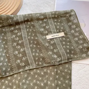 Macro detail of olive green floral cotton linen scarf with an explore infinity woven label
