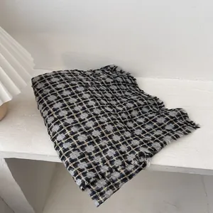 Detailed view of plaid scarf with fringe edges in black, grey and beige woven fabric