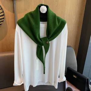 Details des dunkelgrünen Strickschals aus Wolle mit Goldknopf über weißem Top